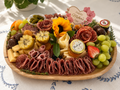 Mother's Day charcuterie board with fruits, cheeses, and flowers on a decorative tablecloth.